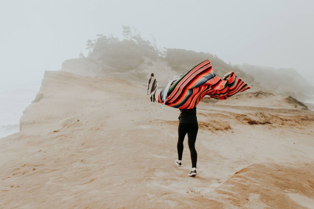 Person walking along a foggy clifftop with a striped blanket in the wind