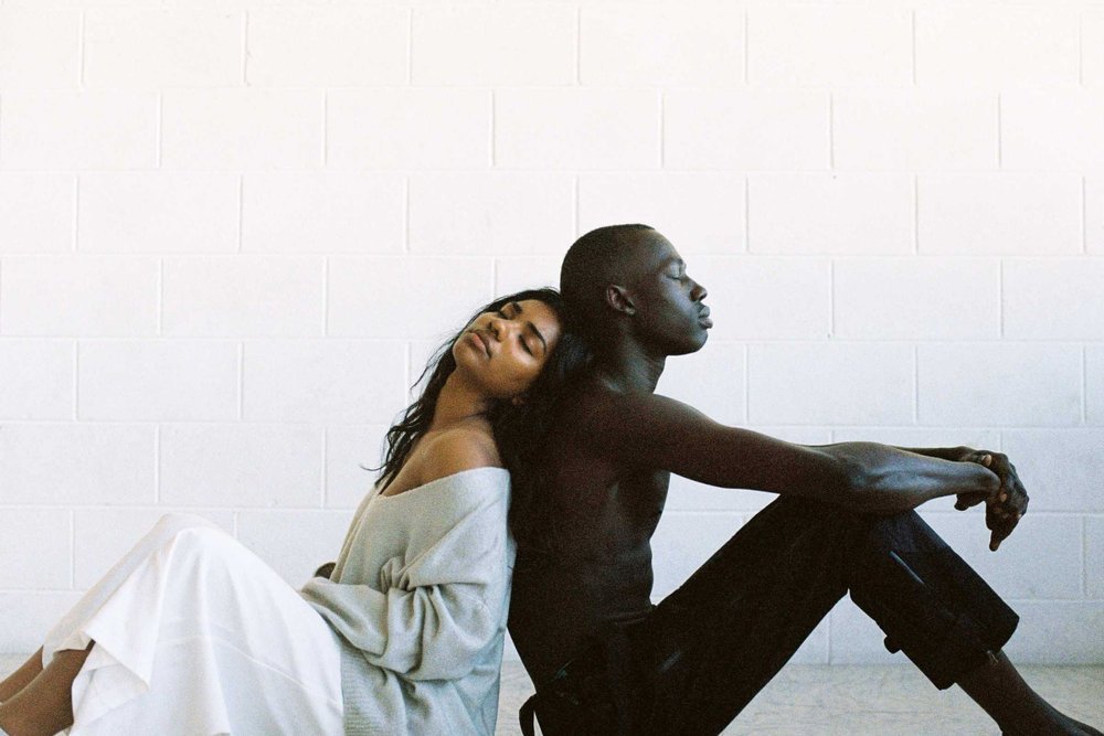 Couple sitting back to back against a white brick wall