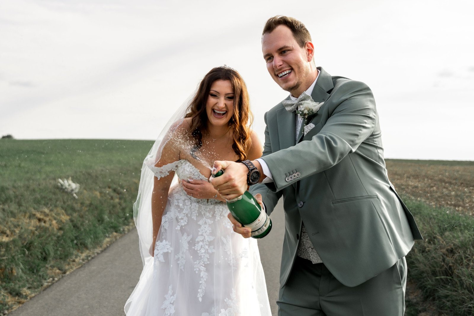 Bride and groom laughing as he pops champagne